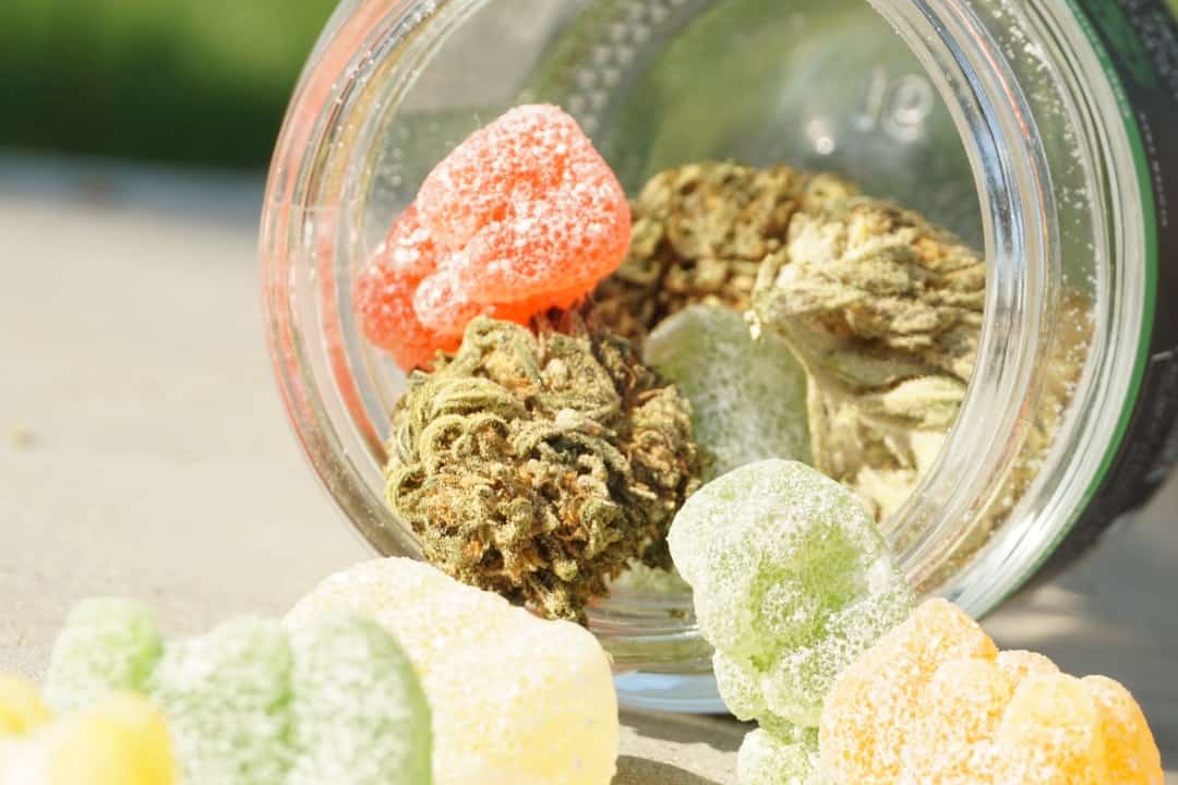 Jar with cannabis buds and colorful gummies