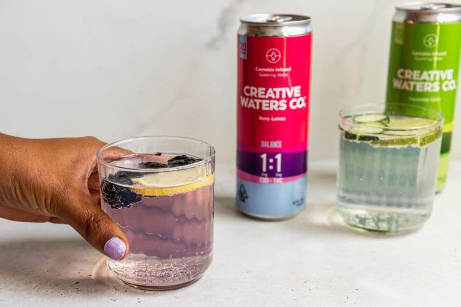 Hand holding berry lemon drink with cans and glasses