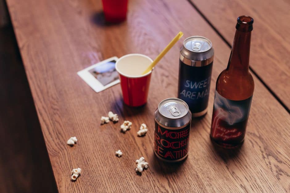 Cans, bottle, cup, popcorn on wooden table