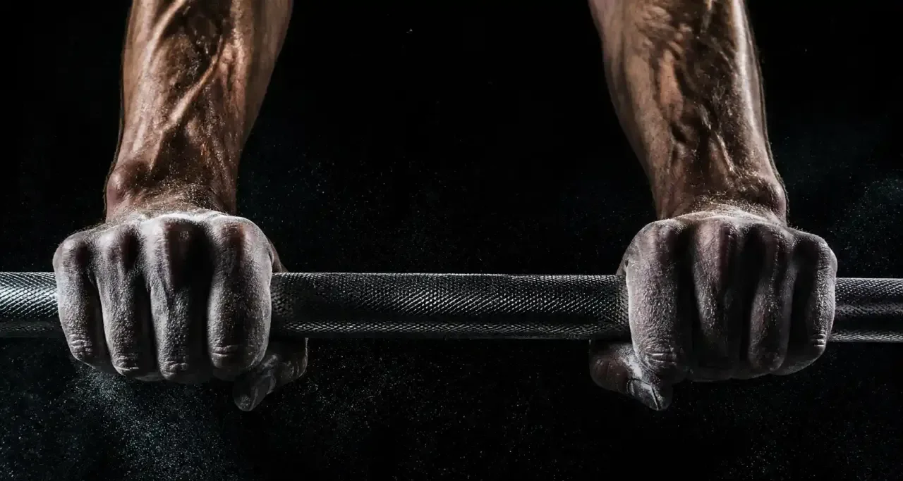 Gros plan de mains recouvertes de magnésie agrippant une barre de musculation