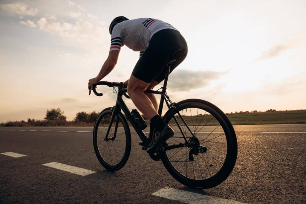 Cyclist riding a bike on an open road at sunset for outdoor activity.