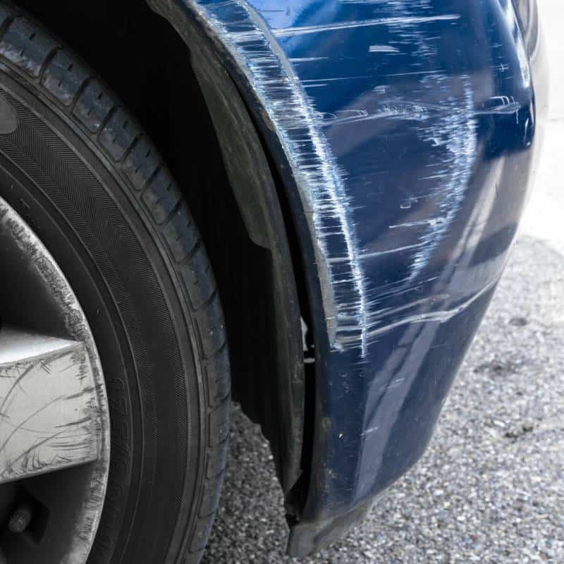 Damaged blue car fender with scratches and dents after an accident.