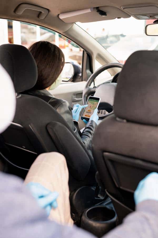 Rideshare driver using a smartphone inside a car during a ride.