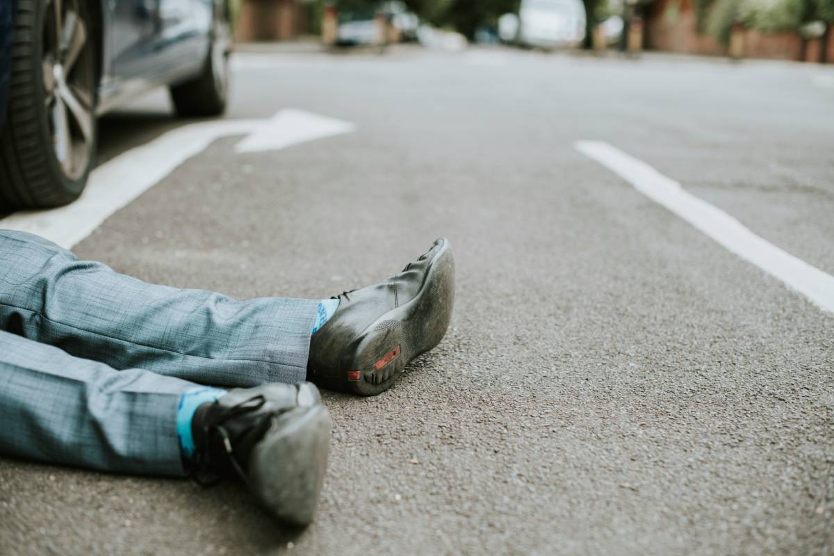 Person injured in pedestrian accident lying on the road with a car nearby.