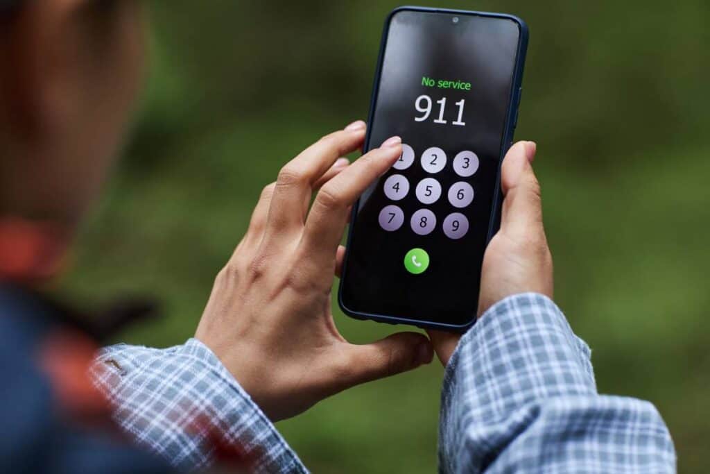 Person dialing 911 on a smartphone in an outdoor setting.