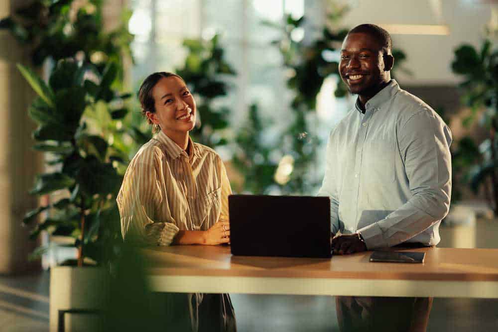 Two professionals standing at a table reviewing information on a laptop during a leadership clarity conversation.