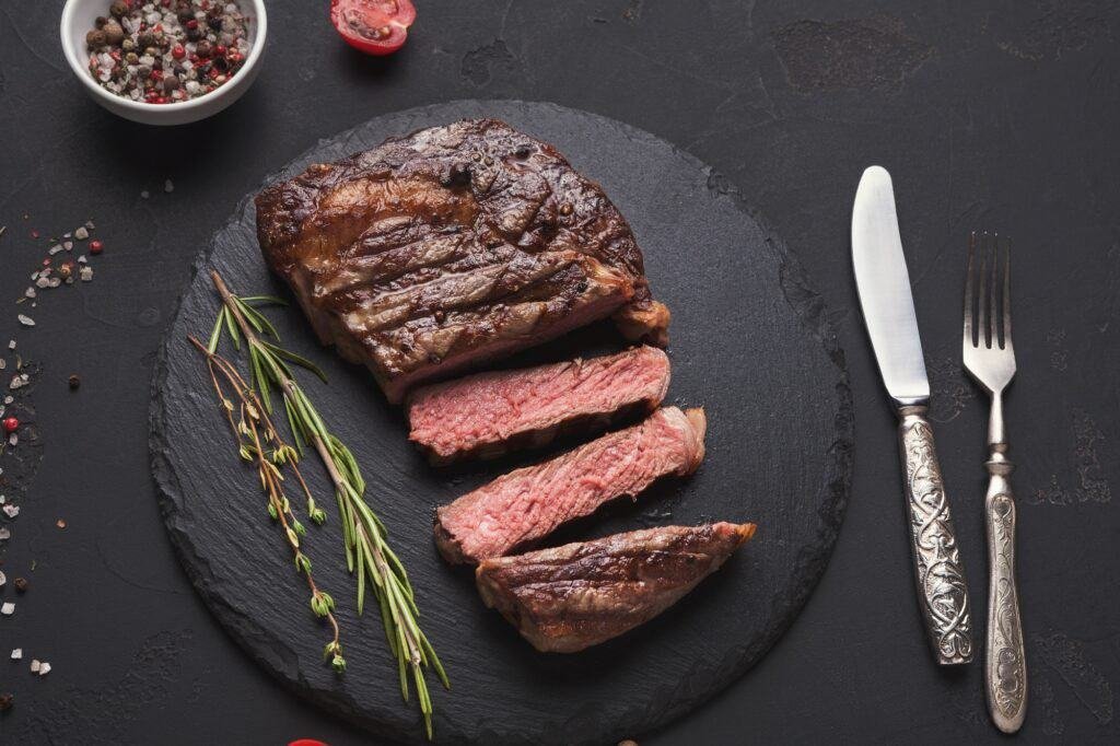 Rib eye steak and spices on black background