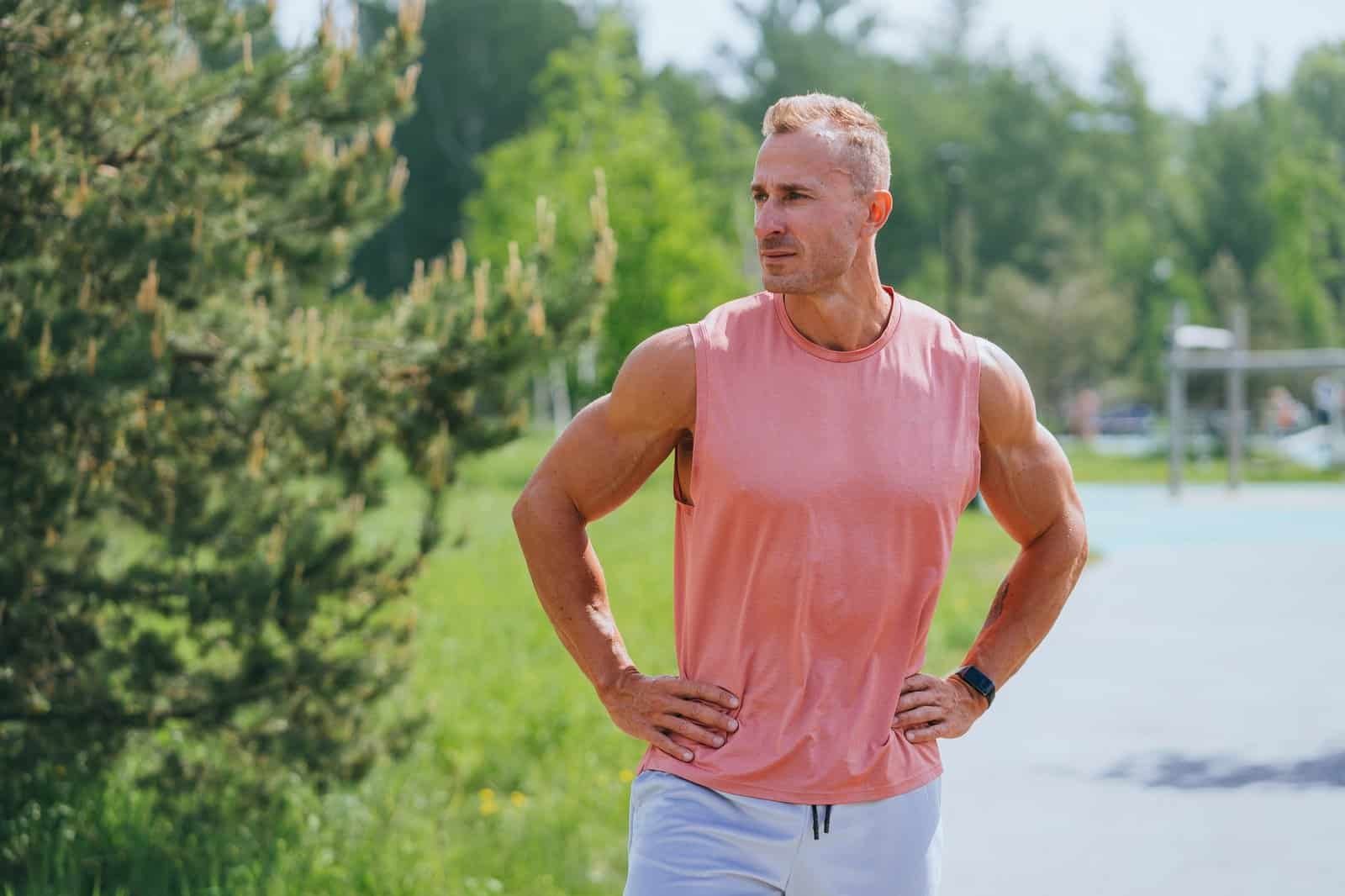 Strong man in hormonal balance in sportswear standing looks aside, tired after workout