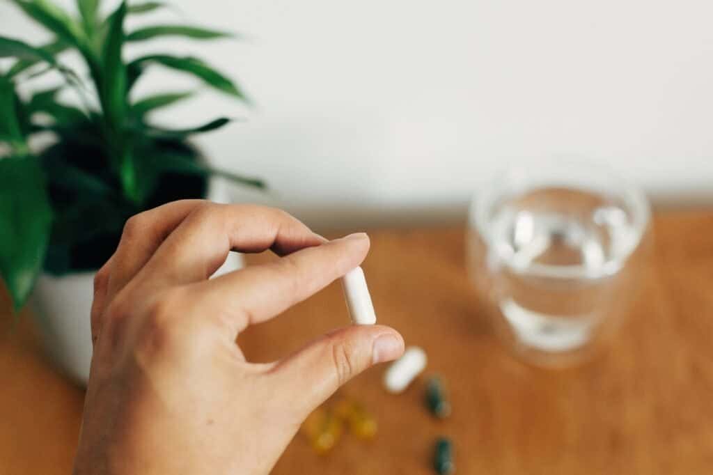 Hand holding magnesium capsule above glass of water on wooden table