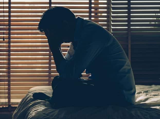Depressed man sitting on bed with head in his hands