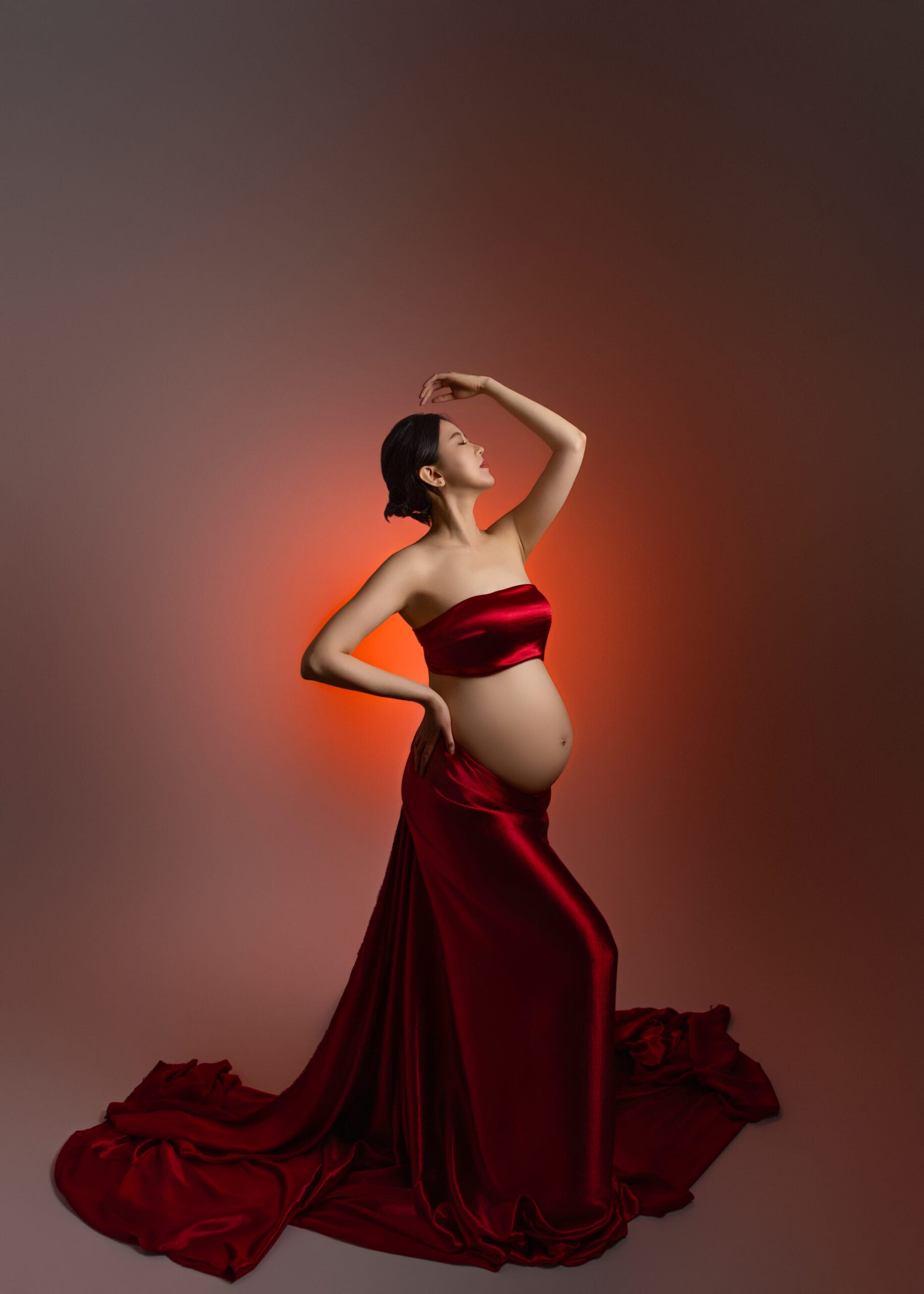 timeless maternity photoshoot with mom wearing red dress with red lighting coming from her back
