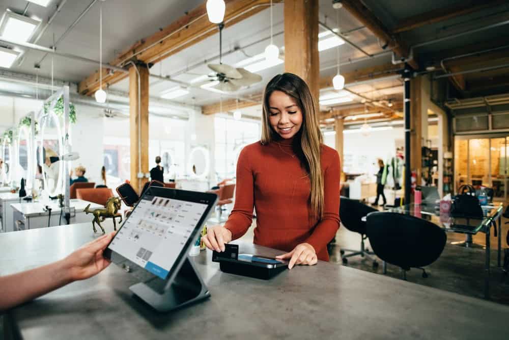 Girl using tablet at cafe in modern co-working space, friendly customer service, coffee shop workspace, casual business meeting, technology in hospitality, professional customer interaction.