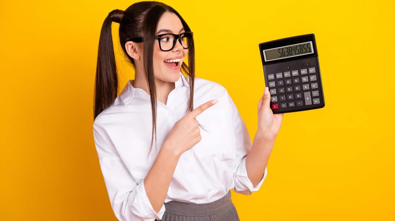 Calculator with large display and woman pointing at it on bright yellow background.