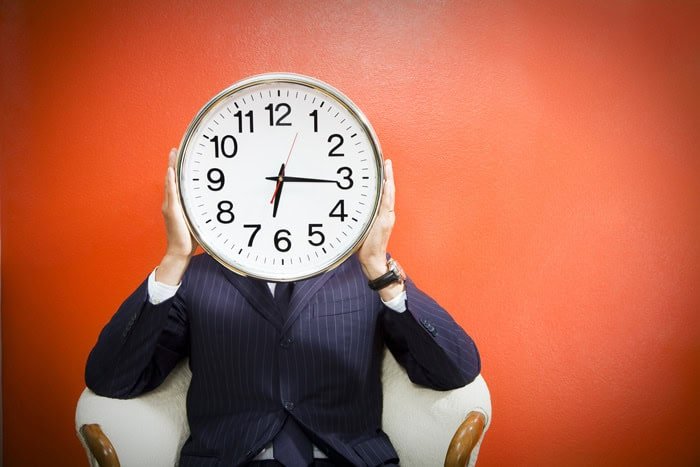 Clock featuring the time 2:15 held by a person in business attire against a red background.