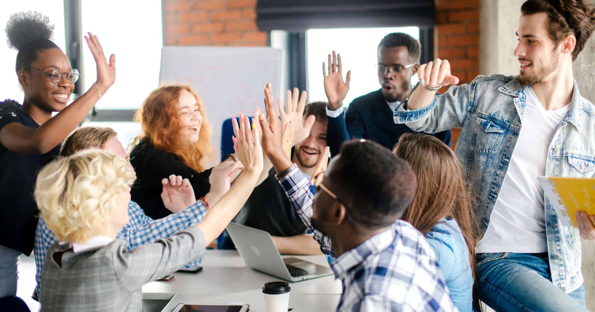 High-energy team meeting with diverse colleagues giving high fives and celebrating success in a modern office environment.