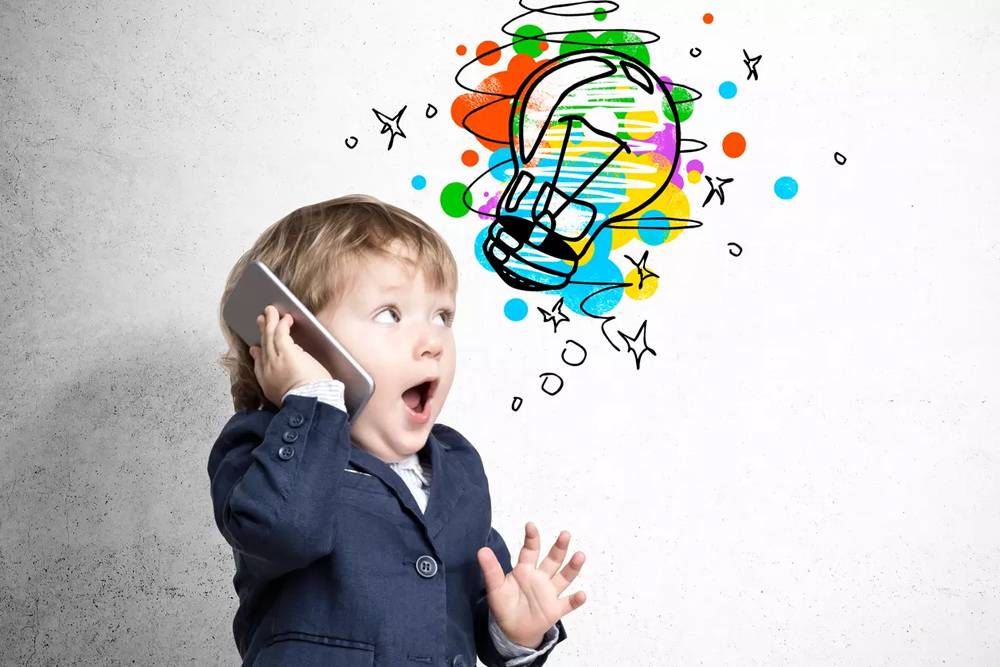 Colorful doodle of a light bulb with paint splashes and stars above a surprised young boy talking on a smartphone, representing creativity and innovative ideas.