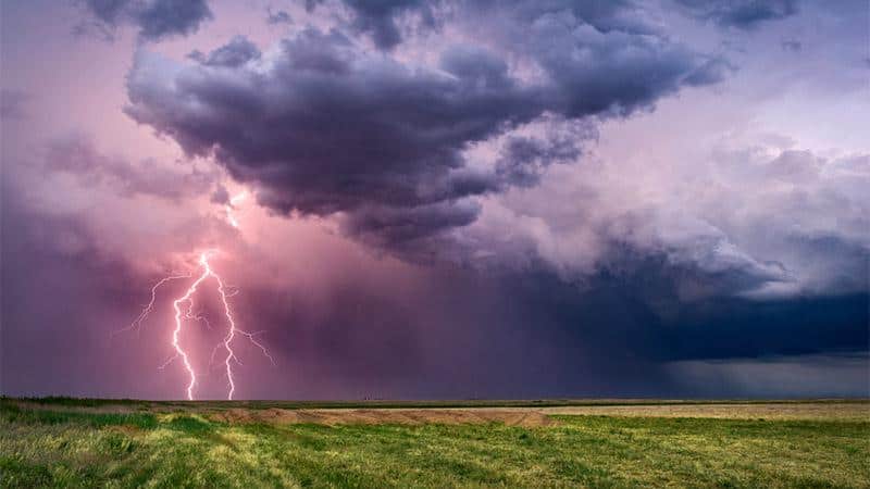 Lightning storm over open field with dark dramatic clouds and vibrant sky, striking lightning, weather photography, natural disaster images, Chris Hood.