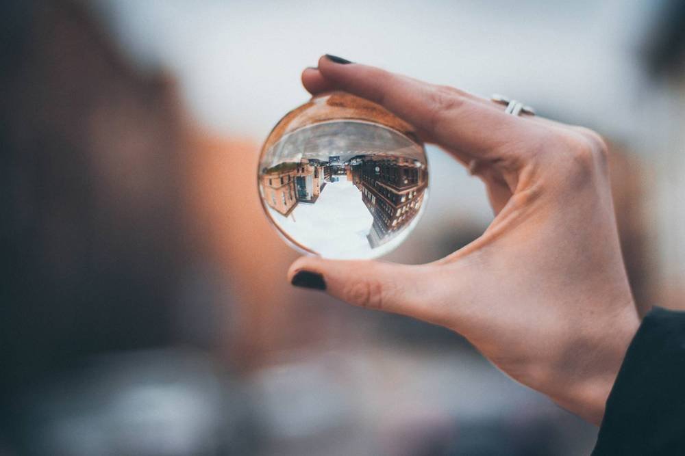 Reflection of city buildings through a glass sphere held by a person’s hand in an urban setting, highlighting photography, creative perspective, and cityscape themes.