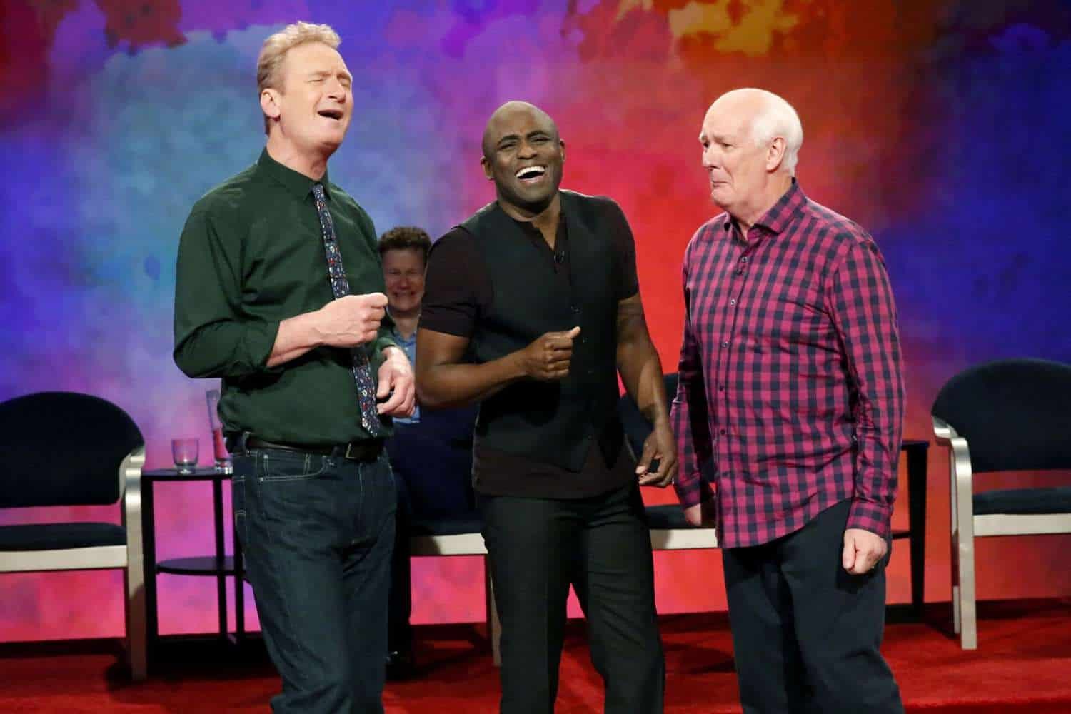 Lively scene from the game show featuring three men laughing and enjoying the moment, with colorful background, emphasizing entertainment and comedy.