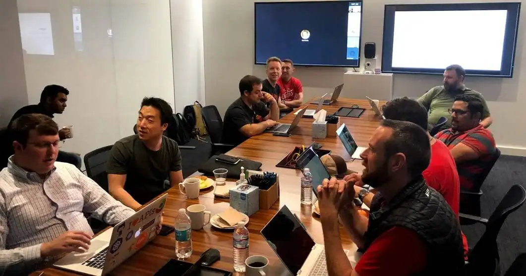 Meeting of diverse team discussing projects at conference table with laptops and presentation screens, modern business office, collaboration, teamwork, technology work environment, digital professionals.