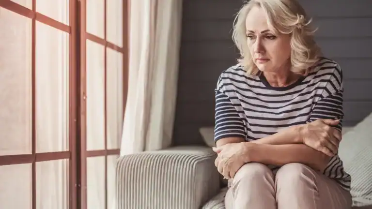 A sad looking woman sitting on a couch with her arms folded in front of her, in need of saying and accepting to herself: God loves you!