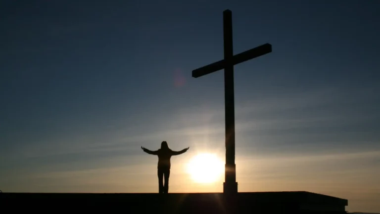 A christian woman standing in front of a cross with her arms raised