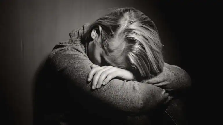Black and white photo of a woman bent over with her head in her arms symbolizing why it feels like God has betrayed you.