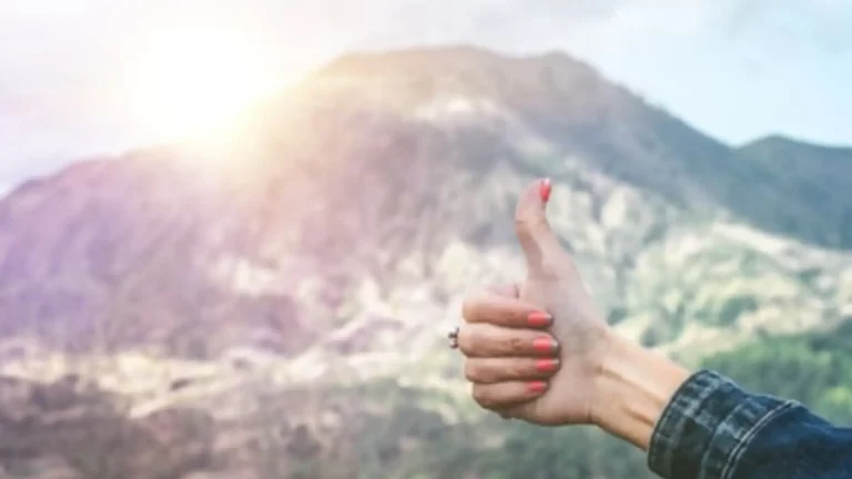 A Christian woman's arm and hand giving a thumbs up in front of a mountain with the sun rising above it symbolizing that God has not given up on you.