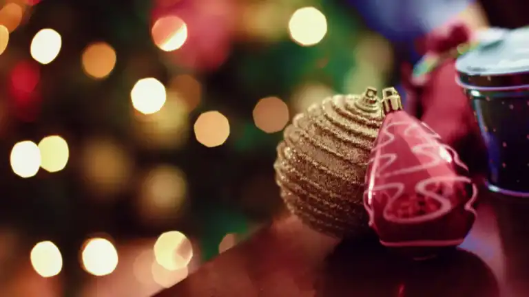Christmas ornaments in the foreground with Christmas lights in the background.
