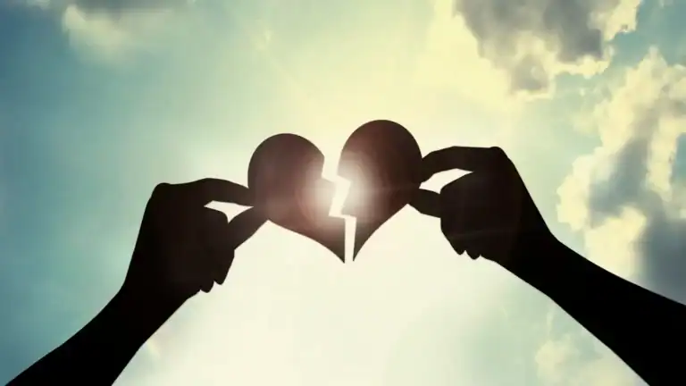 Two hands holding up a broken paper heart in front of the sun. no-pin-it