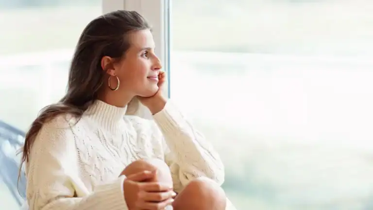 A Christian woman looking out a window smiling relating living out your identity.