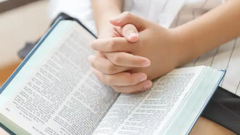 A woman's hands clasped in prayer on top of a Bible