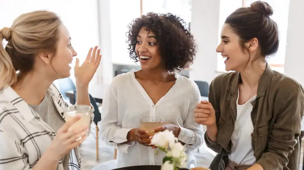 Three women in a Christian women's group talking to one another in a cafe holding drinks.