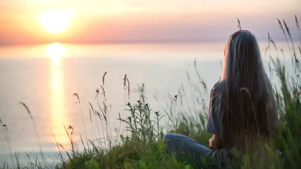 A woman sitting by the water looking at a sunset