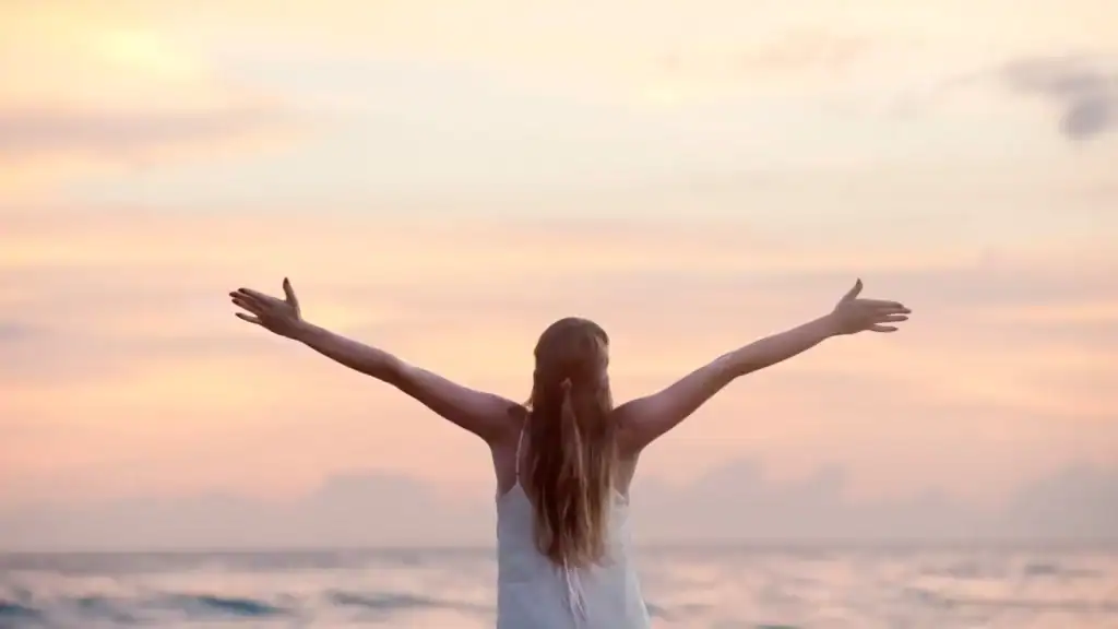 A woman standing with her arms open in front of a lake
