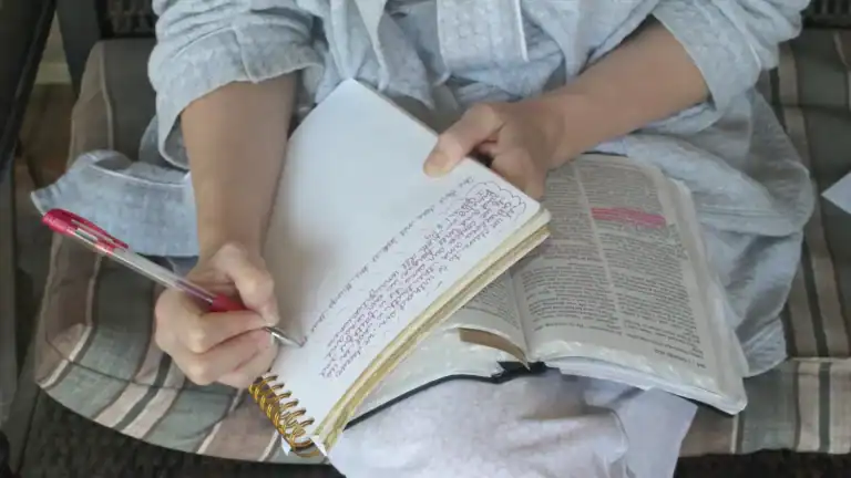 A woman sitting with a Bible and notebook on her lap, writing in the notebook symbolizing inductive bible study method.