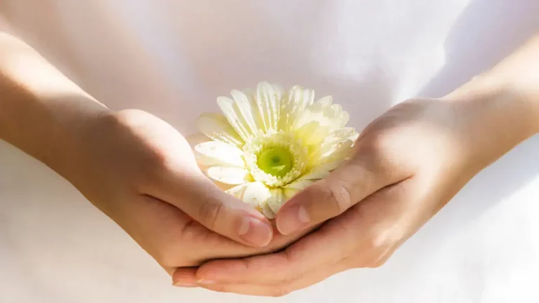 A Christian woman holding a daisy in both hands inviting you to share your blessings