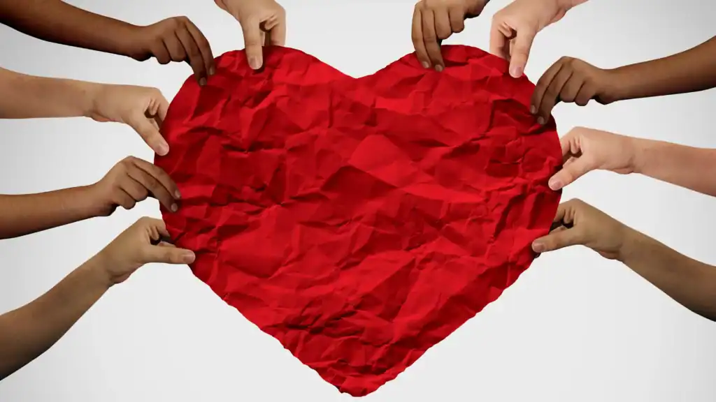 A group of people's hands from all different cultures, holding a red paper heart, symbolizing unity in Christ