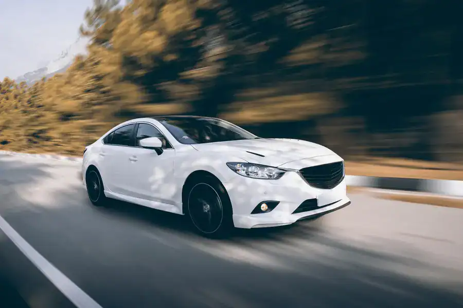 High-performance white sedan driving on a scenic road, emphasizing automotive innovation and quality from CHUHATSU North America, Inc., showcasing expert manufacturing and distribution services.