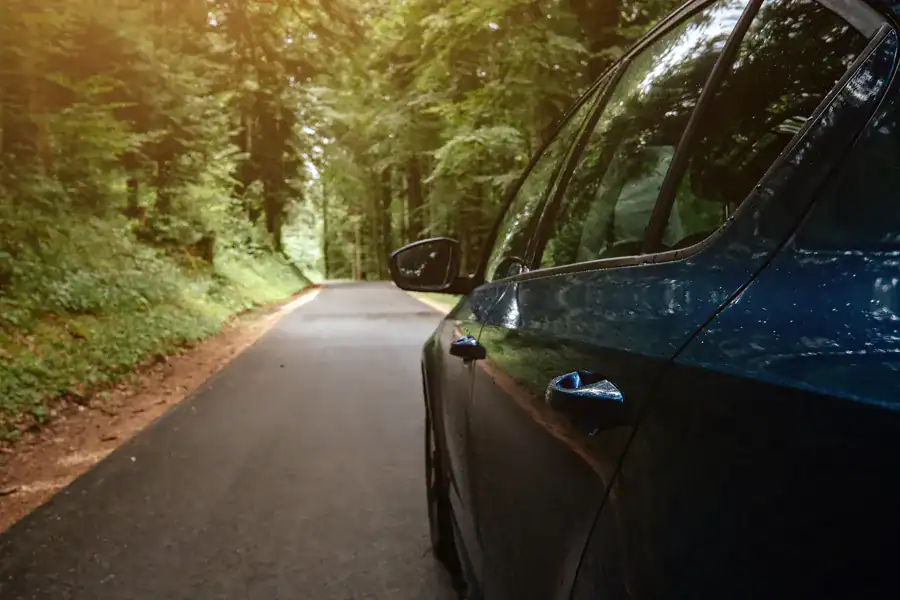 Modern black car parked on a scenic forest road surrounded by lush greenery, emphasizing outdoor adventure and transportation.