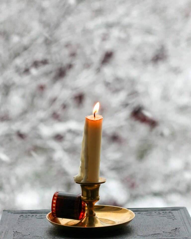 Photo of single candle in a window with snow outside, representing holiday lonliness