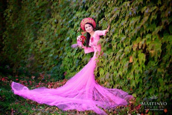 A woman in a pink dress is leaning against a tree.
