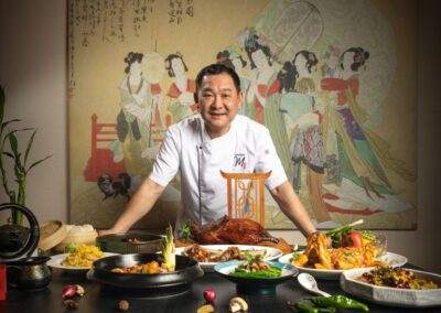 An asian chef standing in front of a table full of food.