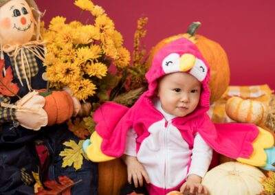 A baby dressed in a pink bird costume surrounded by pumpkins.