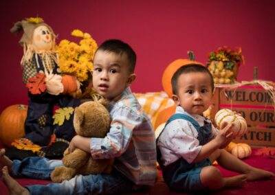 Two boys sitting on a red background with pumpkins and teddy bears.