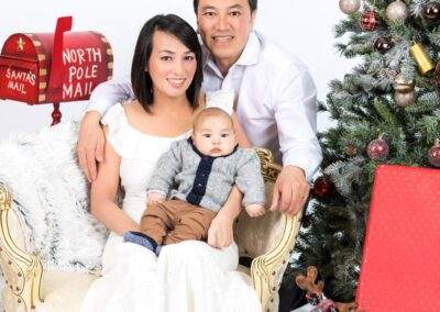 A man and woman pose with a baby in front of a christmas tree.
