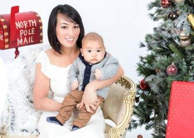 A woman holding a baby in front of a christmas tree.