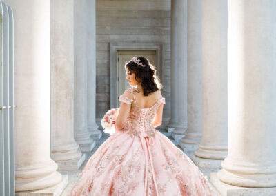 A woman in a pink ball gown is standing in front of pillars.