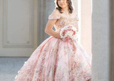 A young woman in a pink dress is posing in front of pillars.