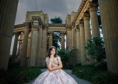 A girl in a pink dress is posing in front of pillars.